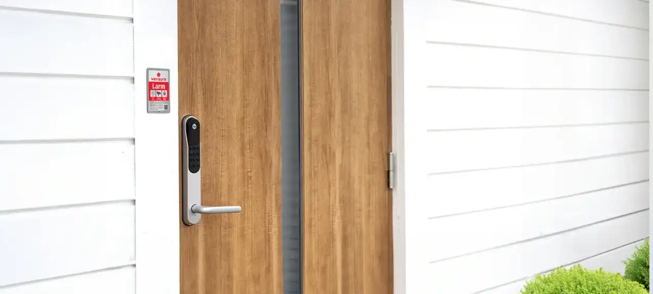 En modern ytterdörr med ett Verisure smart låsmodul installation. Dörren är i trä och husfasaden är vit.