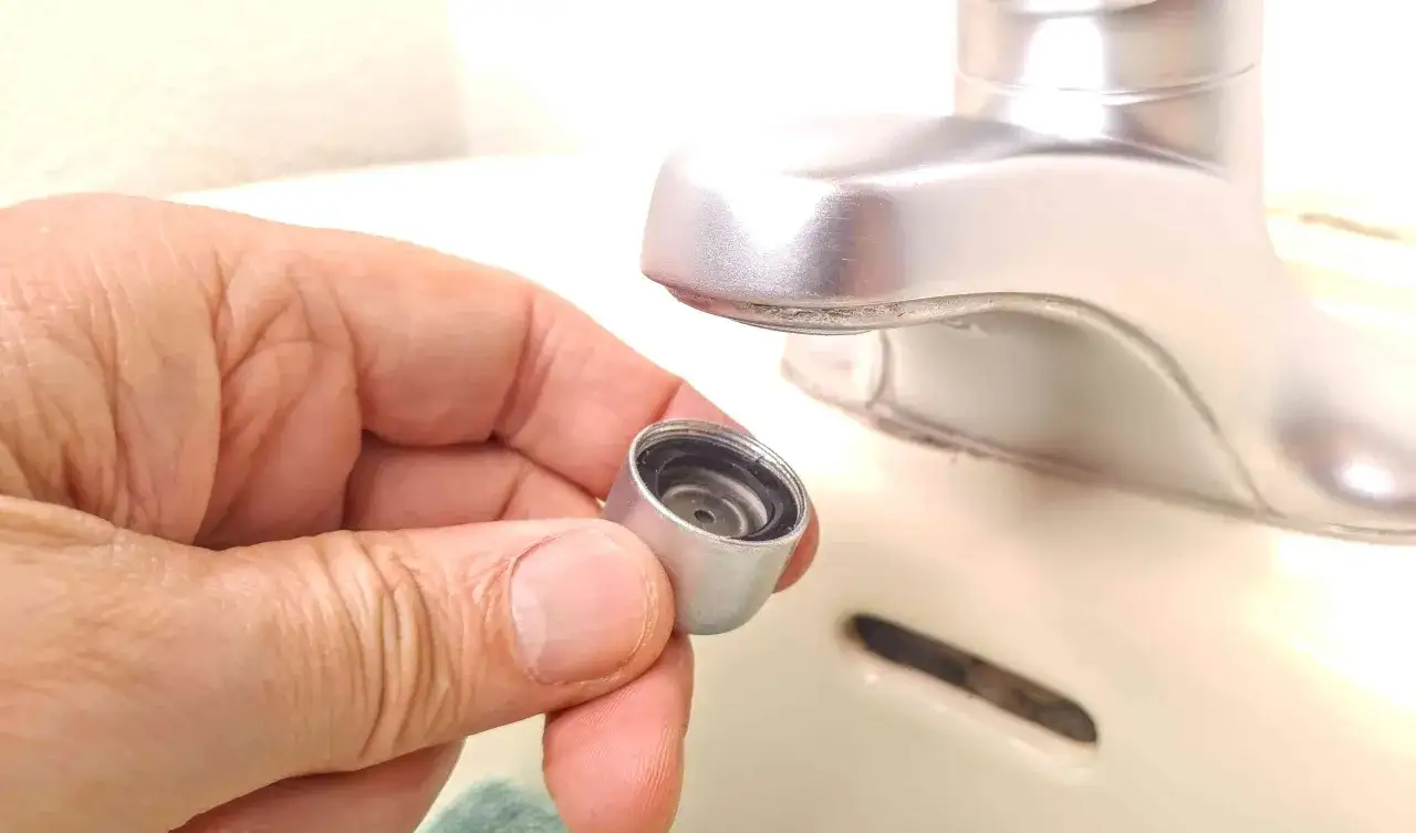Main tenant une pièce de robinet démontée, une étape pour comment réduire la pression d'eau sur un robinet.