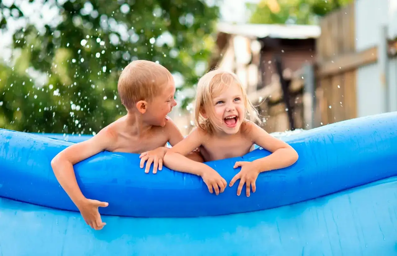 Niños riendo y chapoteando en una piscina inflable azul, disfrutando de juegos refrescantes.