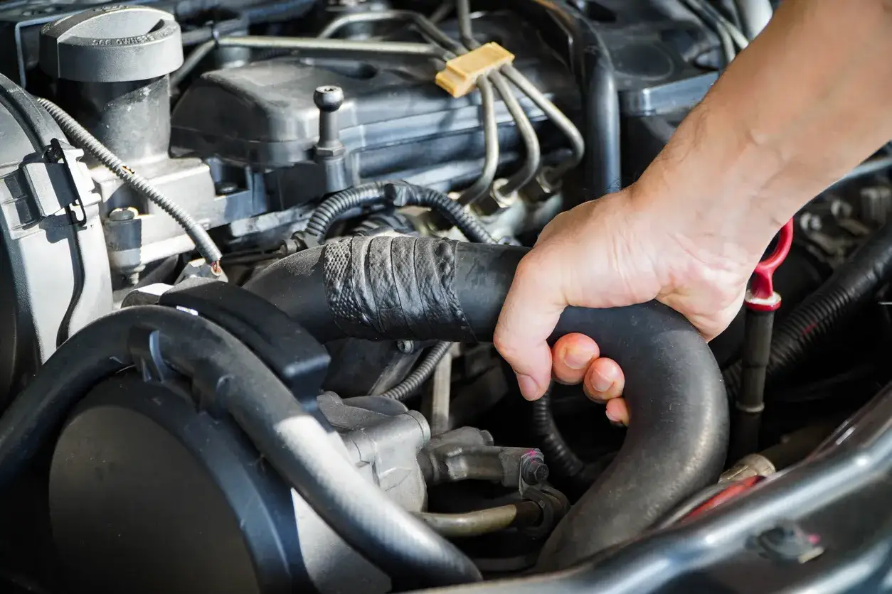 Main d'un mécanicien inspectant une durite turbo percée, réparée avec du ruban adhésif noir, dans un compartiment moteur.