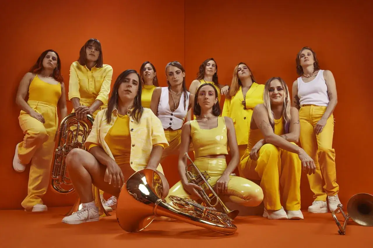 Un gruppo di donne con abiti gialli, pronte a suonare musica balcanica con ottoni scintillanti.