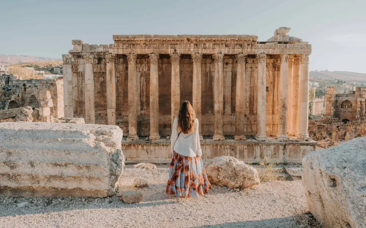 A woman in a flowing skirt stands before ancient Roman ruins, a testament to past days in Lebanon.