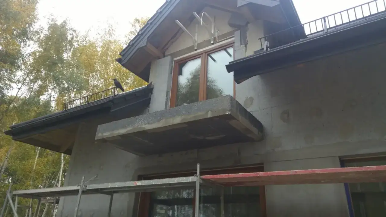 Trwa termomodernizacja budynku. Widać rusztowania, niedokończony balkon i ptaka na dachu.