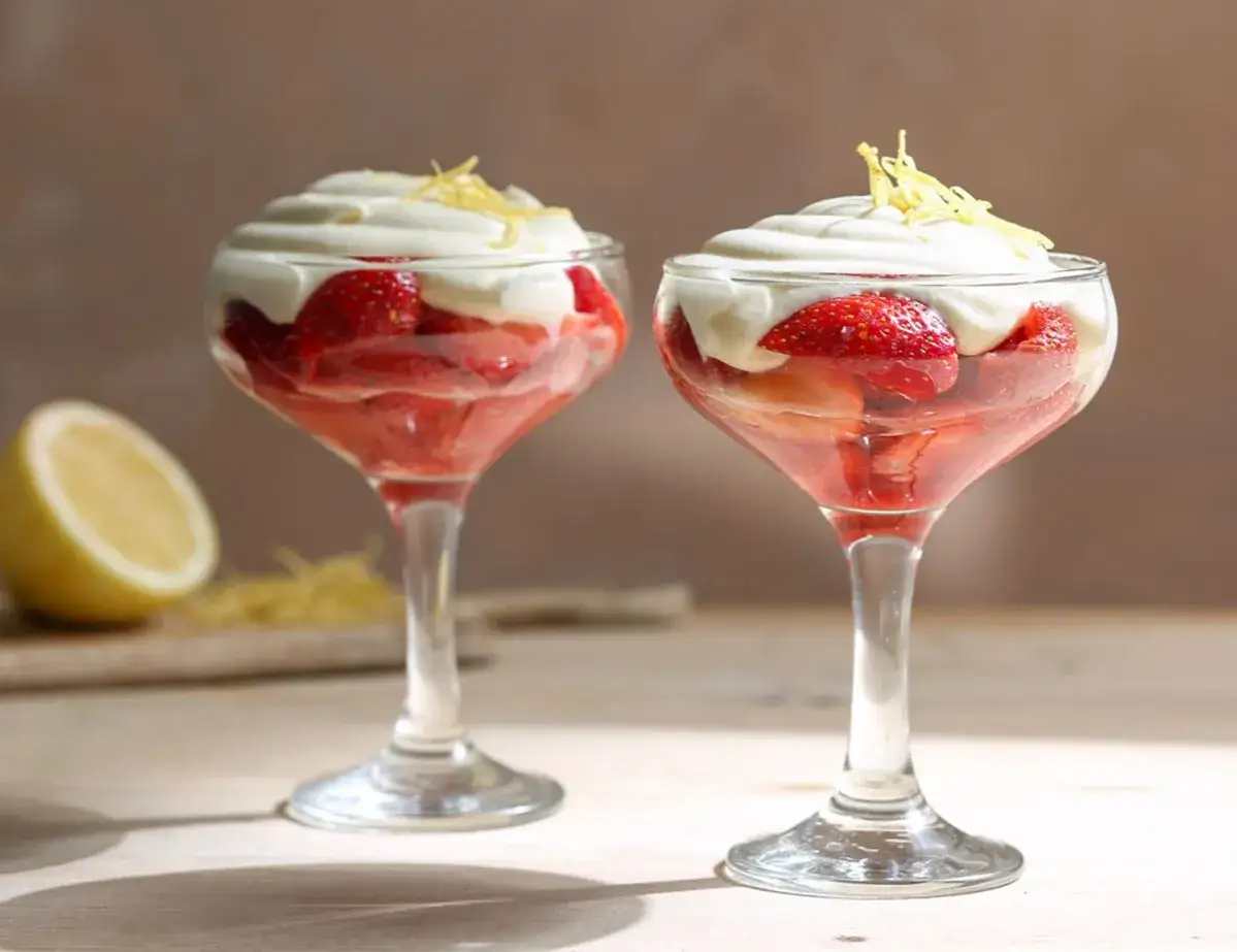 Zwei Gläser mit Erdbeeren, Sahne und Zitronenzesten. Ein erfrischendes Dessert, das an eis mit Sekt erinnert.