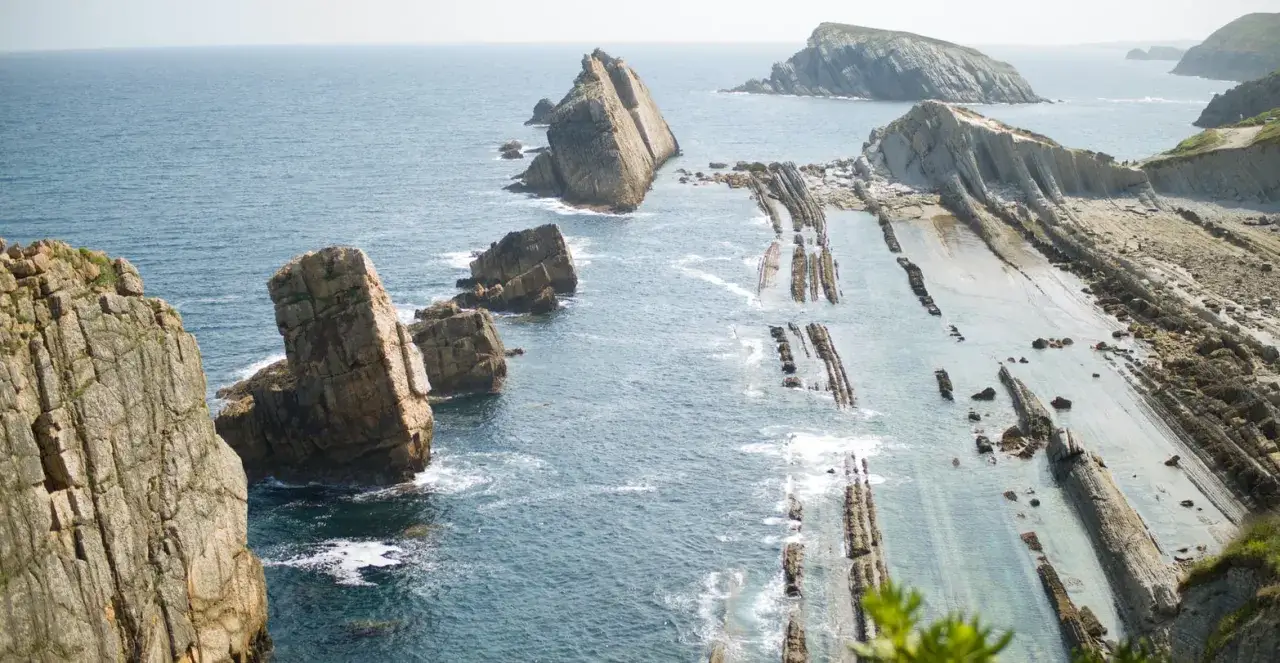Dramatic rock formations and layered strata of the flysch de Zumaia coastline meet the blue ocean, showcasing nature's geological artistry.
