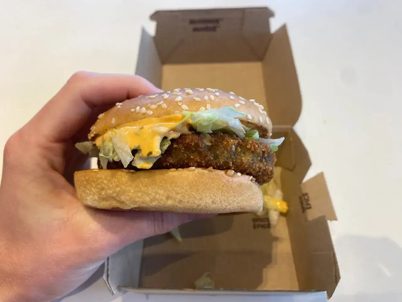 Ręka trzyma wege burgera z McDonald's, w pudełku widać resztki sosu. Ciekawe, ile ma kcal.