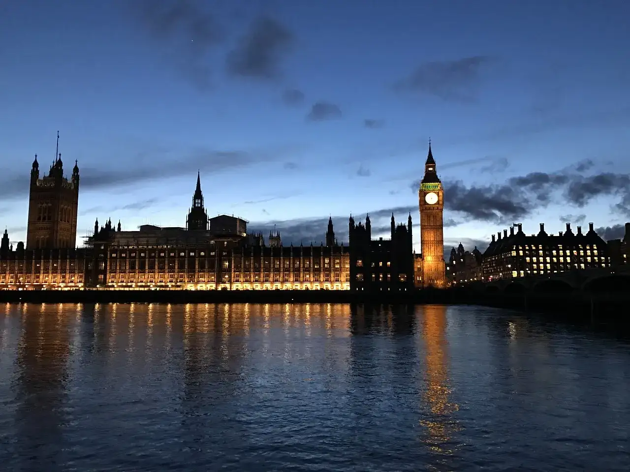 Iconico Big Ben e il Palazzo di Westminster illuminati di notte, con riflessi sull'acqua del Tamigi. Londra by night, un incanto.