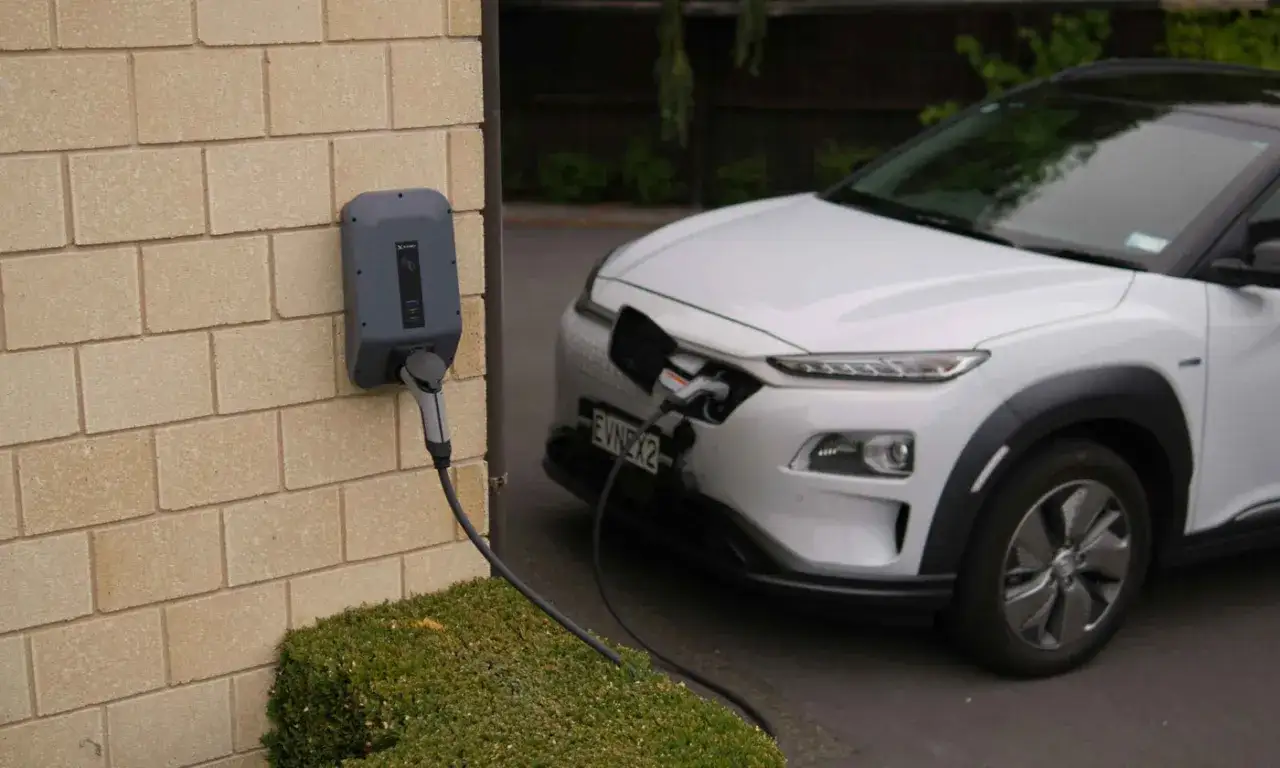 Borne de recharge murale connectée à une voiture électrique blanche. Le frais réel d'une voiture électrique est de plus en plus accessible.