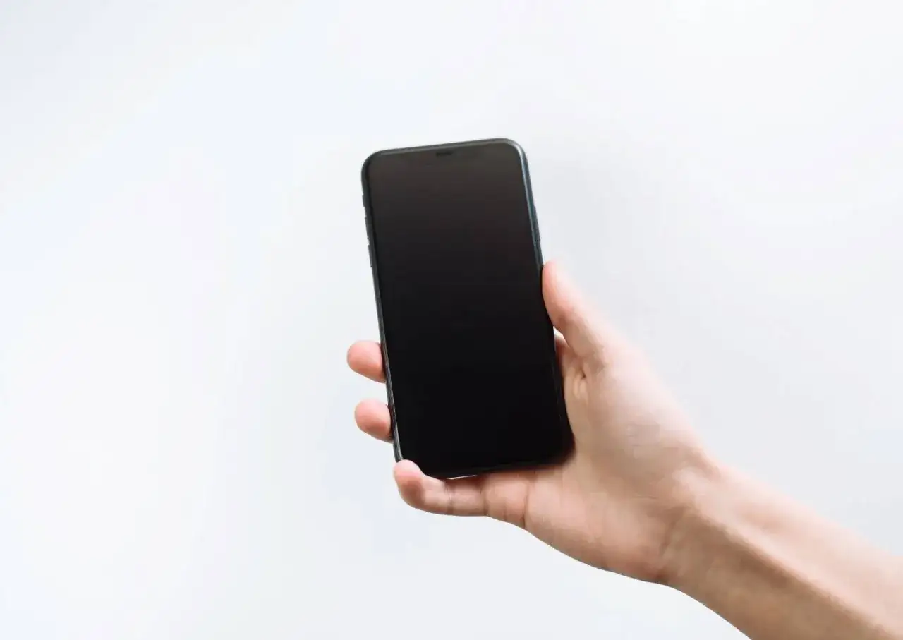 Dłoń trzyma smartfon z czarnym ekranem w telefonie.