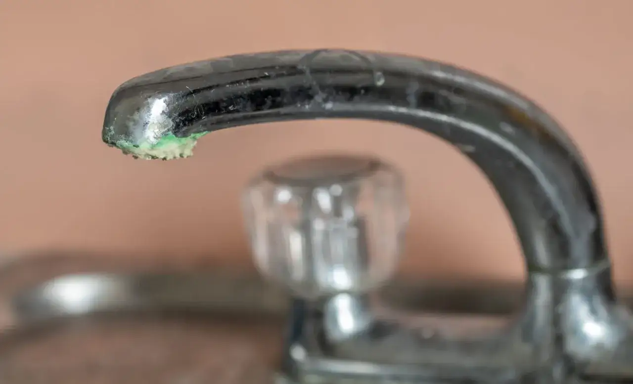 Gouttelettes d'eau et dépôts verts sur un robinet, signe qu'il faut éliminer le calcaire.