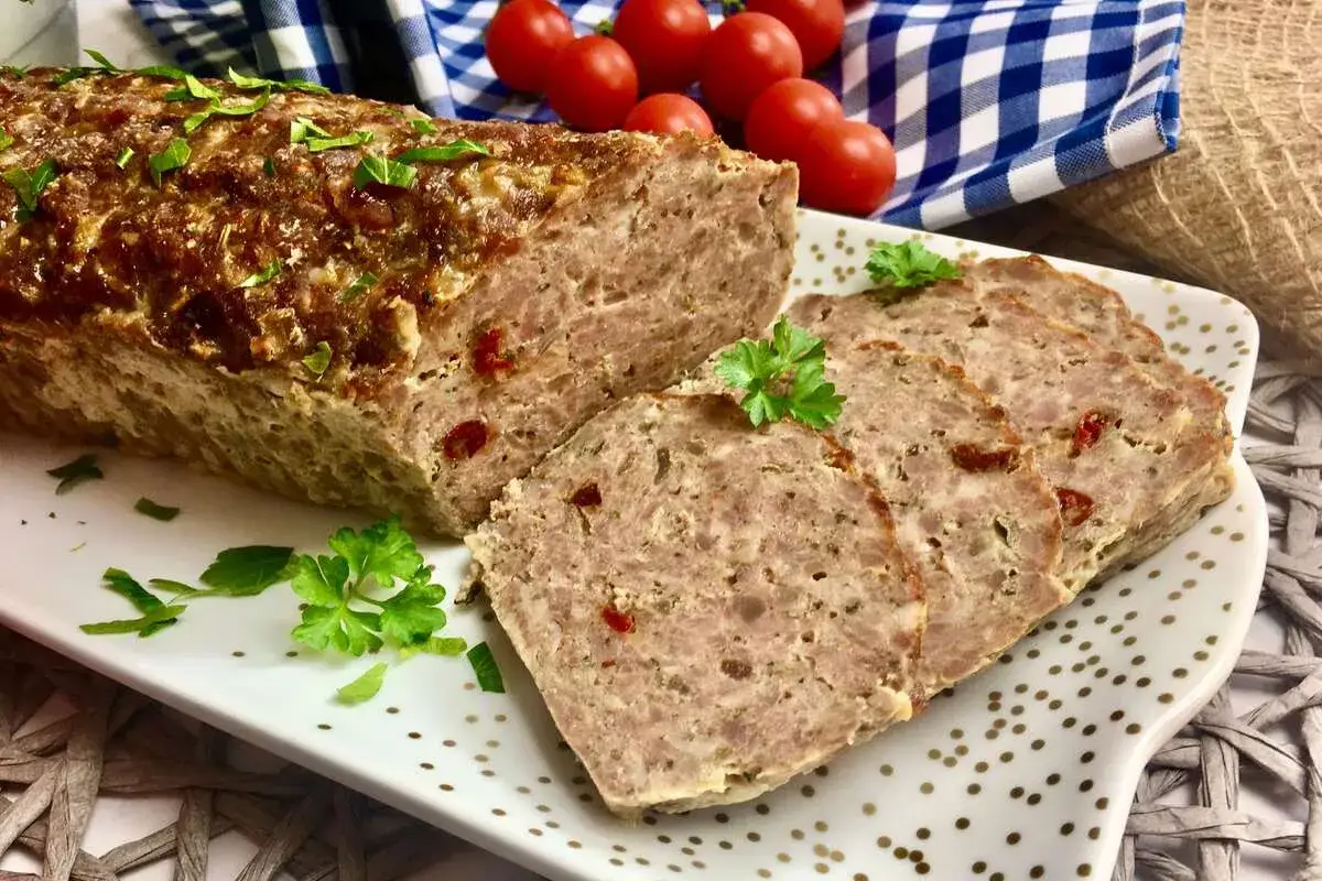 Pyszna pieczeń z mięsa mielonego, idealna na kanapki. Pokrojona w plastry, ozdobiona natką pietruszki, z pomidorkami w tle.