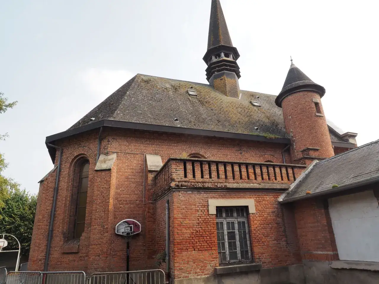B&acirc;timent en briques rouges avec une tourelle et un clocher, peut-&ecirc;tre l'&eacute;cole Jean de Saint-Venant. Un panier de basket est visible.