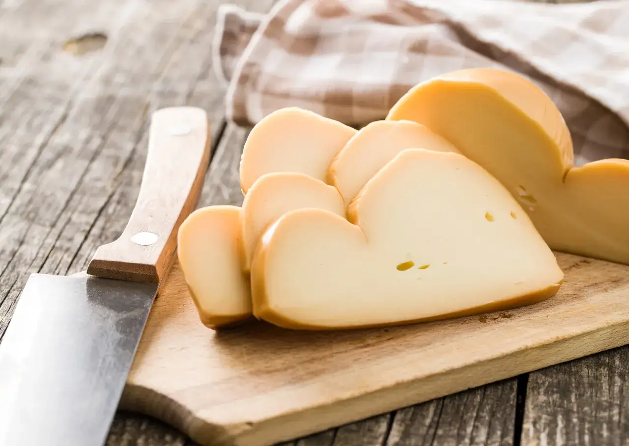 Fette di provola affumicata su tagliere di legno, accanto a un coltello.