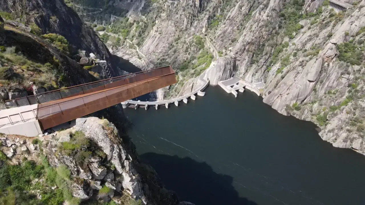 El mirador del fraile se proyecta sobre un embalse, con una presa de hormigón y montañas escarpadas.