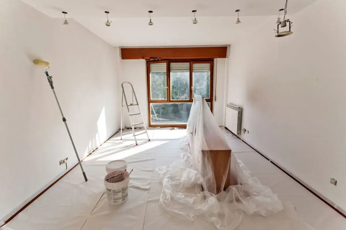 Un rouleau à peinture, une échelle et des pots de peinture sont prêts pour peindre cette pièce. Le mobilier est protégé par une bâche.
