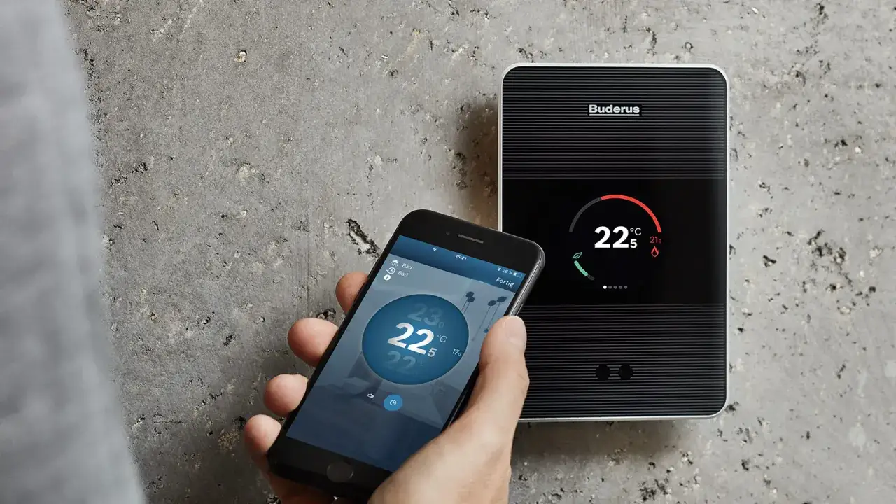Smartfon z aplikacją Buderus pokazuje temperaturę, podczas gdy obok urządzenie grzewcze wyświetla komunikat o błędzie A11.