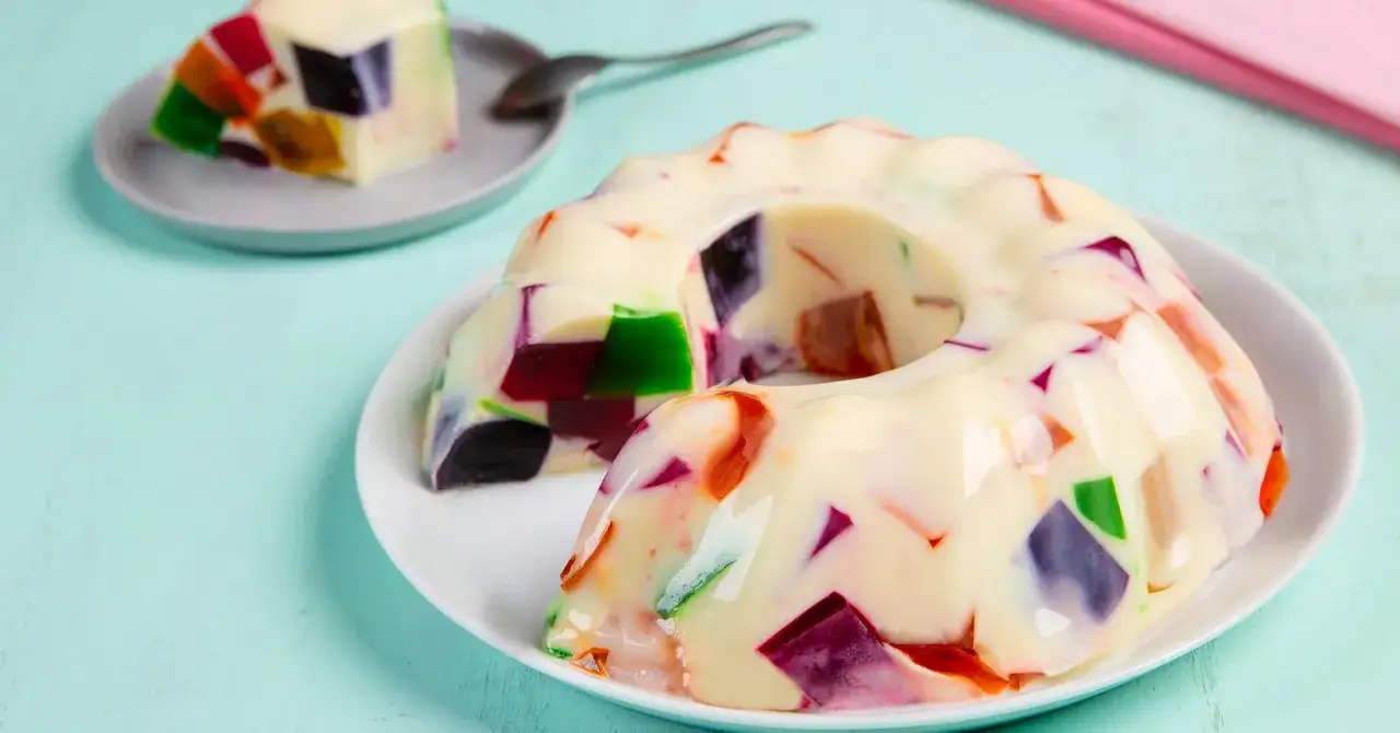 Postre de gelatina con leche condensada, con trozos de gelatina de colores vibrantes incrustados.