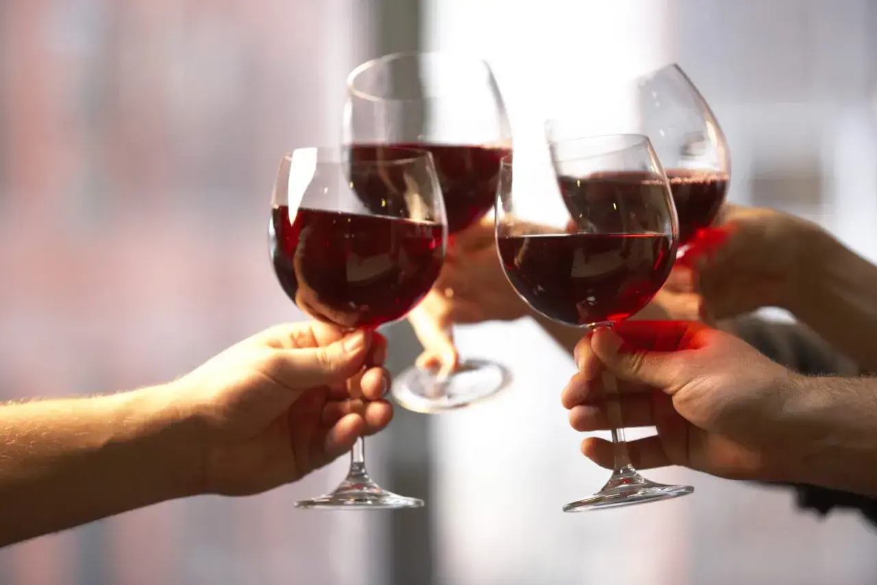 Quatre mains portent des verres de vin rouge, leur couleur profonde capturant la lumière. Un toast à la joie.