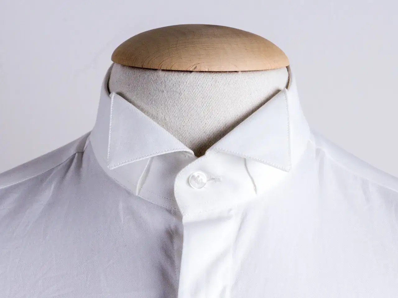 Dettaglio di una camicia bianca su manichino, che mostra i diversi tipi di colletto camicia con un colletto a punta pronunciata.
