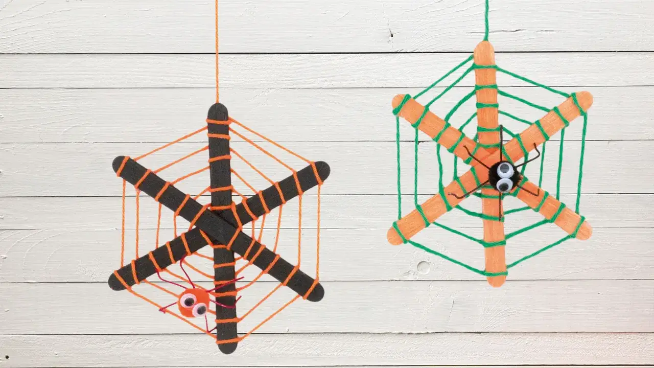 Zwei selbstgebastelte Spinnennetze aus Eisstielen und Wolle, perfekt für Kinder zum Basteln. Ein Netz hat eine kleine orange Spinne, das andere eine schwarze.