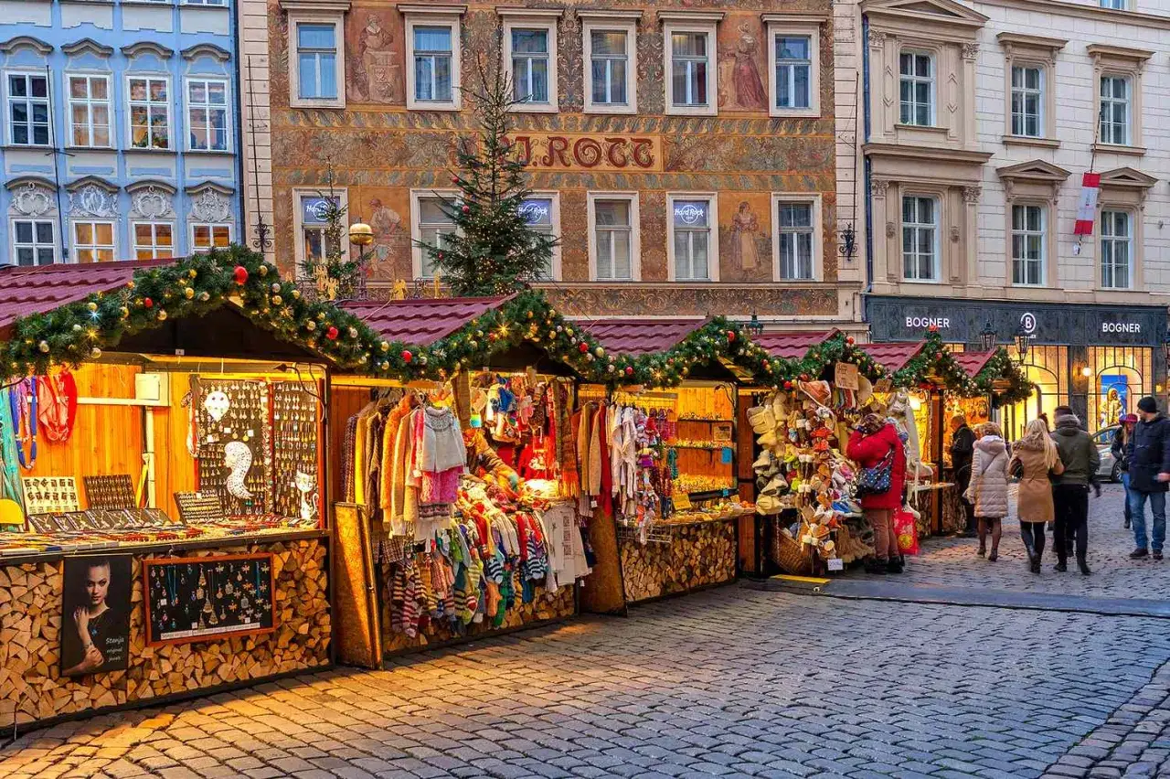 Jarmarki bożonarodzeniowe w Europie: kolorowe stoiska z ozdobami, ubraniami i biżuterią, oświetlone świątecznymi girlandami, na tle zabytkowych kamienic.