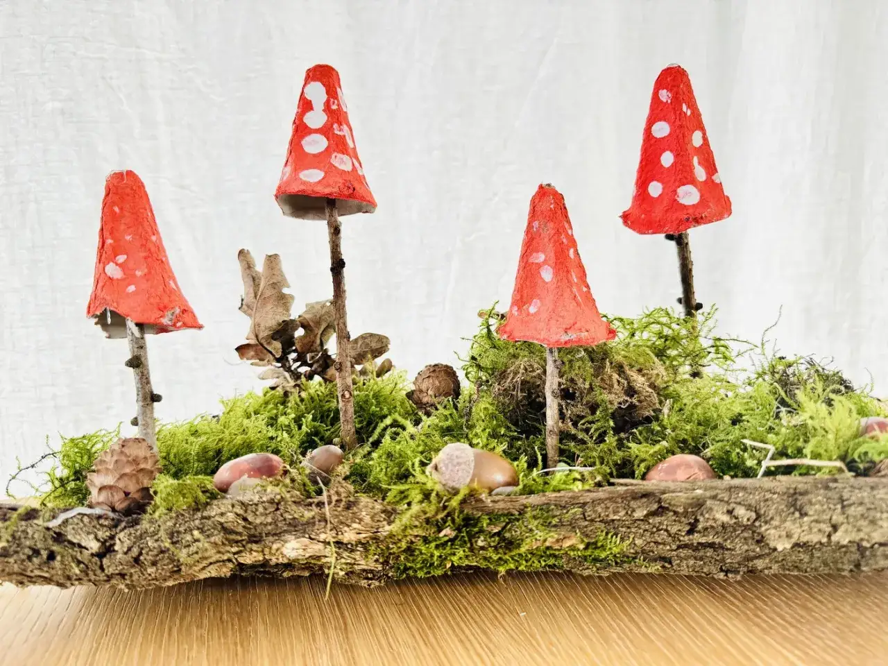 Vier selbstgebastelte Fliegenpilze aus Eierkartons stehen auf Moos und Holz. Ein sch&ouml;nes Beispiel f&uuml;r basteln im Wald mit Kindern.