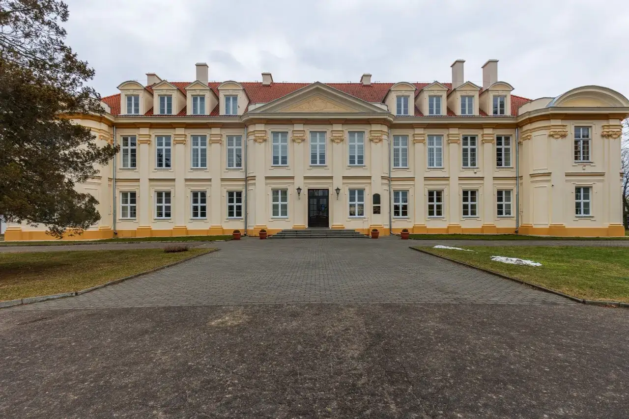 Pałac biskupów kujawskich w Wolborzu, okazała budowla z żółtą fasadą i czerwonym dachem, otoczona zielenią i brukowanym podjazdem.