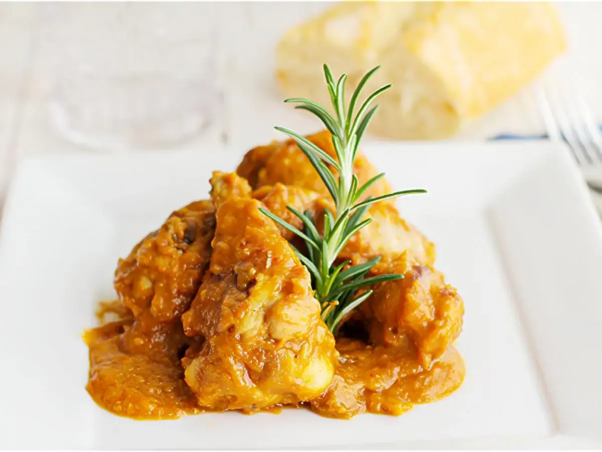 Pollo en salsa de la abuela Carmen, jugoso y tierno, con una ramita de romero. Un plato casero que evoca recuerdos.