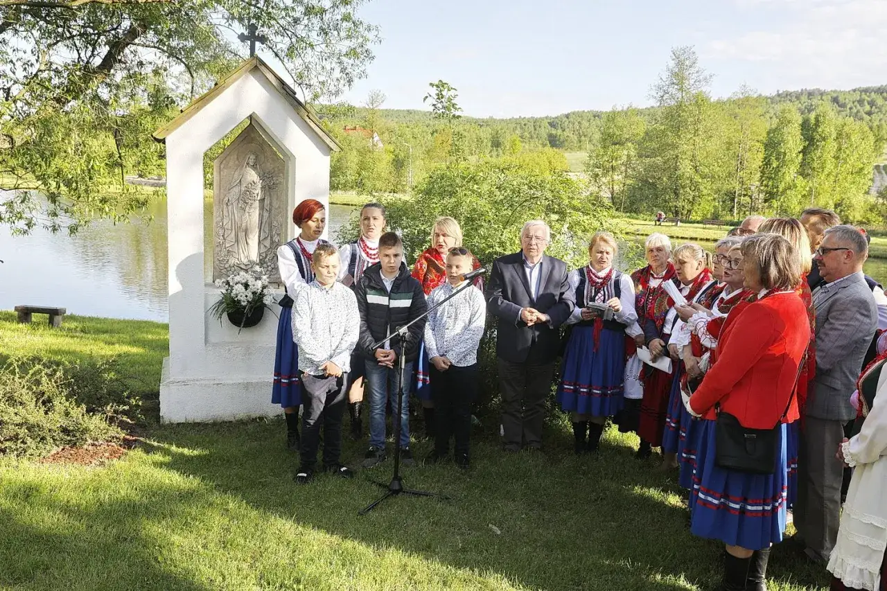 Grupa ludzi w strojach ludowych śpiewa przy kapliczce. Słychać 