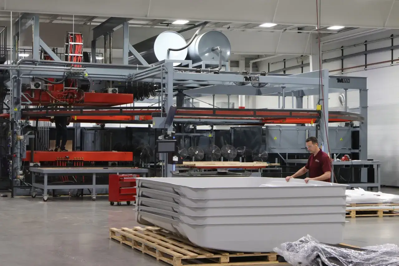 A worker inspects a stack of white polyethylene sheet bathtubs, ready for shipping from the factory.