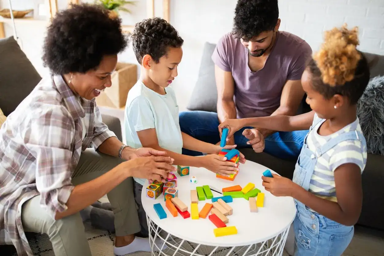 Familia jugando con bloques de colores. La madre sonr&iacute;e mientras los ni&ntilde;os y el padre se concentran en la construcci&oacute;n. &iexcl;Un momento divertido para hacer preguntas para ni&ntilde;as y ni&ntilde;os!