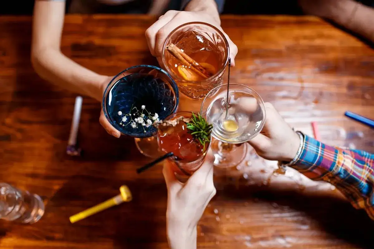 Ręce unoszą kolorowe drinki do toastu. To właśnie co to są shoty – małe porcje alkoholu, idealne na imprezę.