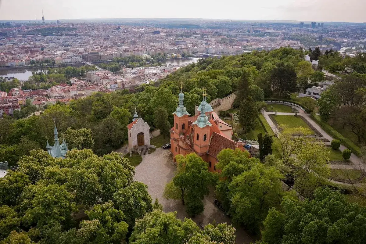 Widok na praską panoramę z wieżą Eiffla w tle. Na pierwszym planie kościół z dwiema wieżami i kapliczka.