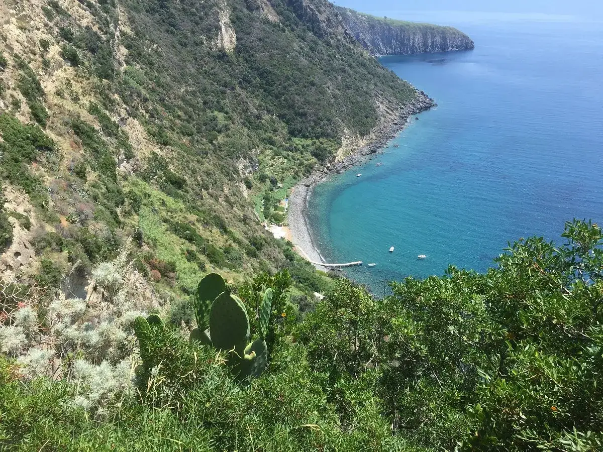 Vista dall'alto della **baia della Scarrupata**, con acque cristalline, una piccola spiaggia di ciottoli e vegetazione mediterranea.