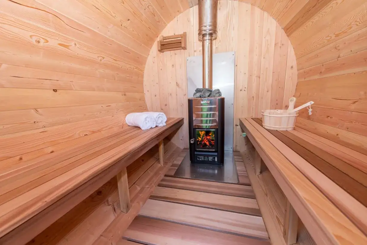 Interior de una sauna de barril de madera con estufas de leña, toallas y cubo. Explora los diferentes tipos de saunas para tu bienestar.