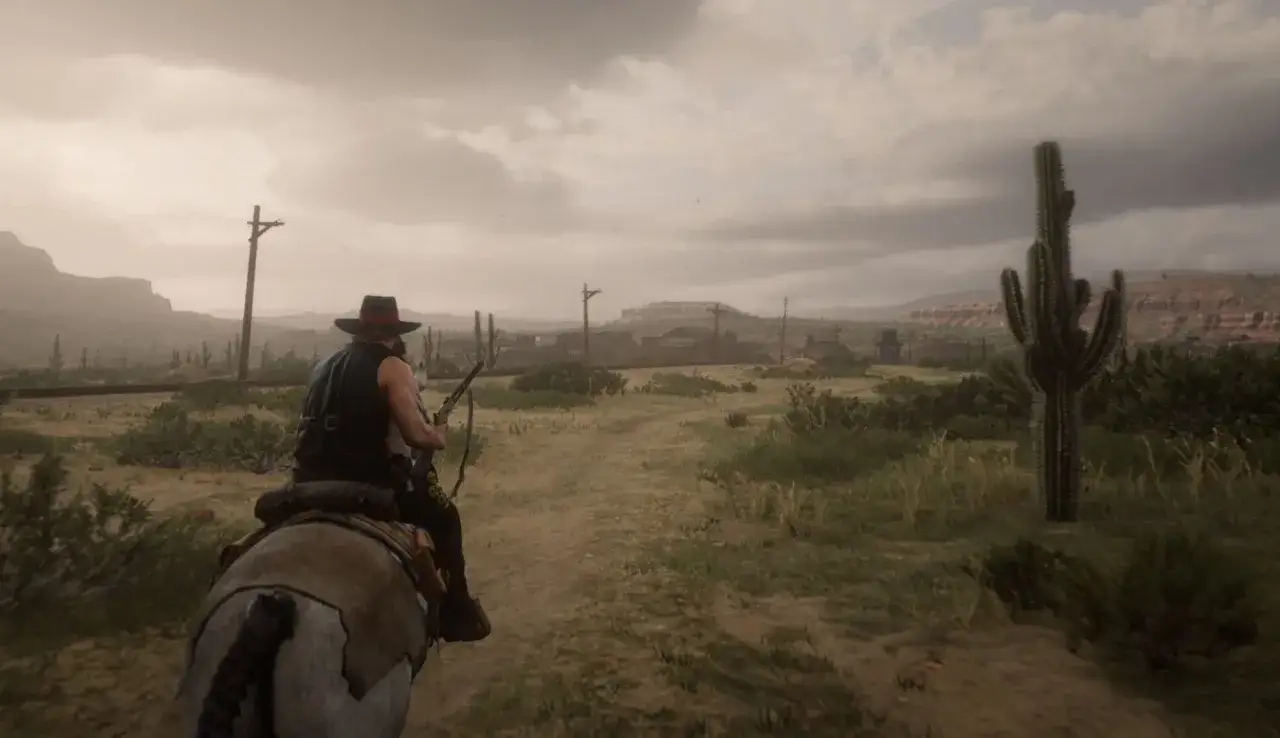 Un cow-boy chevauche dans un paysage d&eacute;sertique, avec des cactus et des poteaux t&eacute;l&eacute;graphiques. L'image est une capture d'&eacute;cran de Red Dead Redemption 2 PC config.