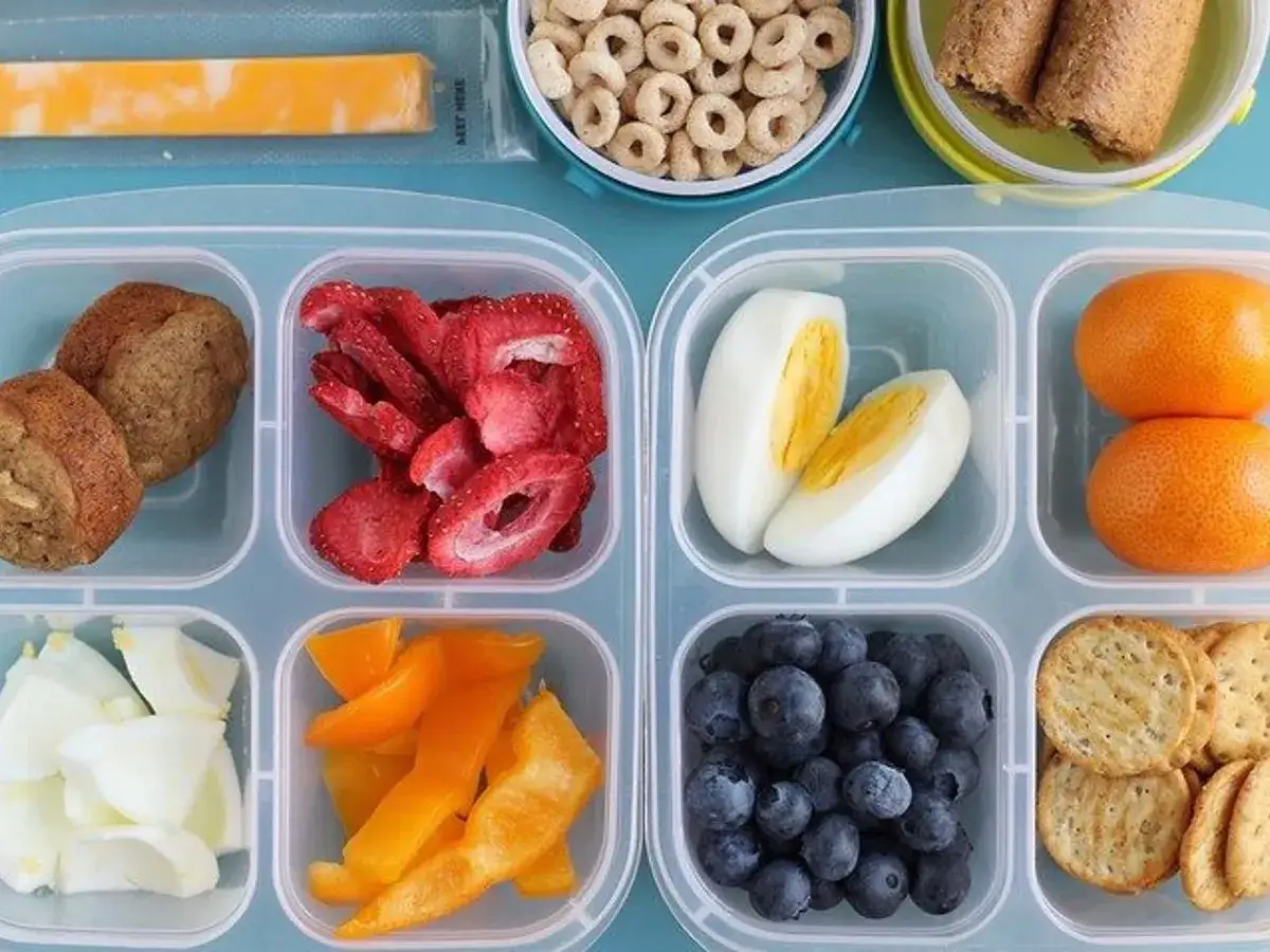 Bento-Box mit kalorienarmen Snacks: Muffins, Erdbeeren, Eier, Mandarinen, Blaubeeren, Paprika und Cracker.