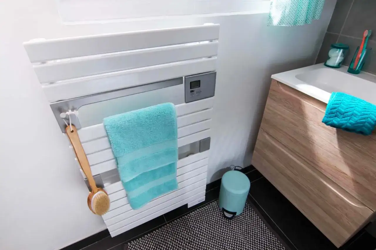 Un s&egrave;che-serviettes blanc moderne avec une serviette bleue. Sa puissance assure un s&eacute;chage rapide et efficace, parfait pour une salle de bain.