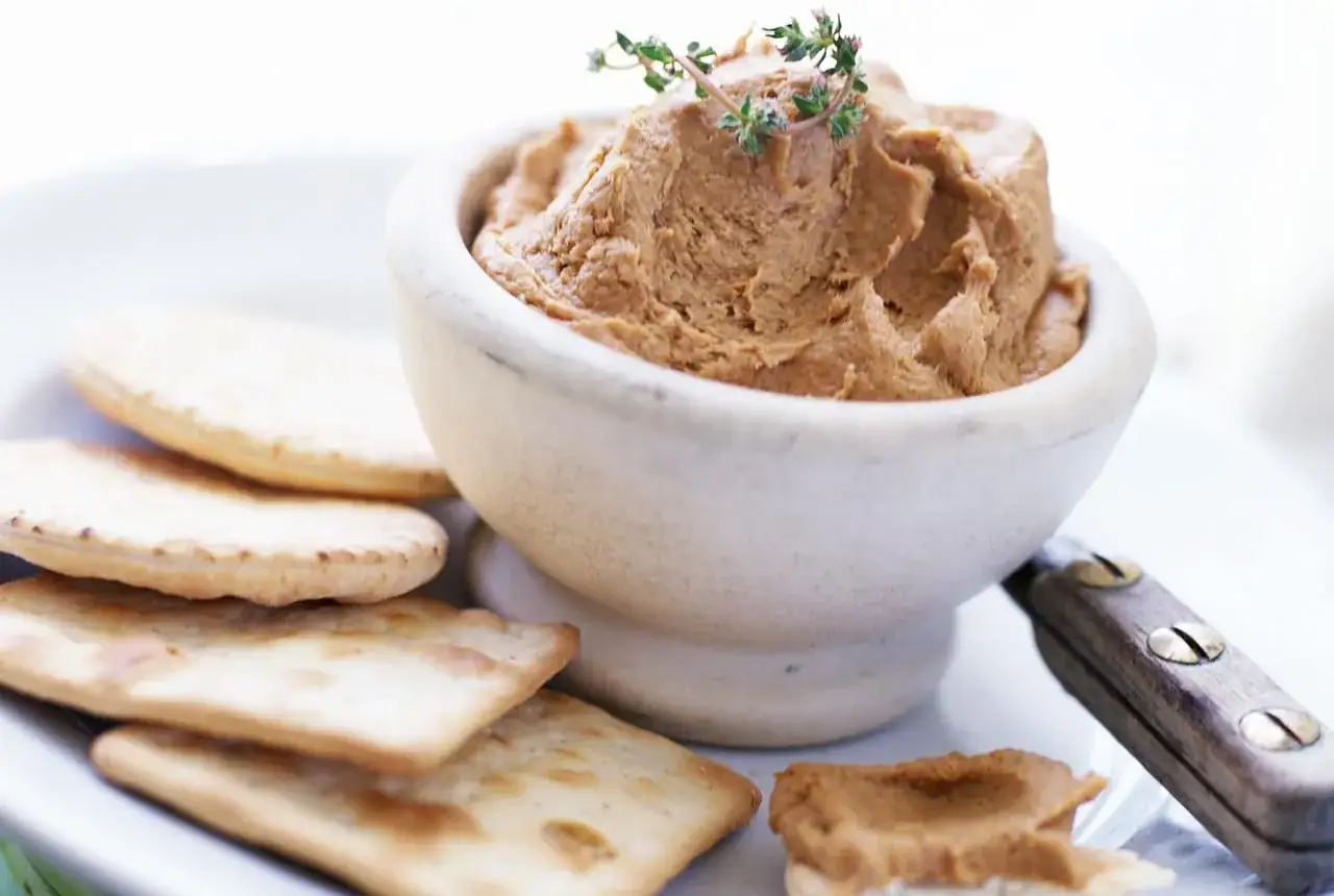 Pate w miseczce, ozdobione gałązką tymianku, podane z chrupiącymi krakersami. Idealna przekąska, która wyjaśnia, pate co to.
