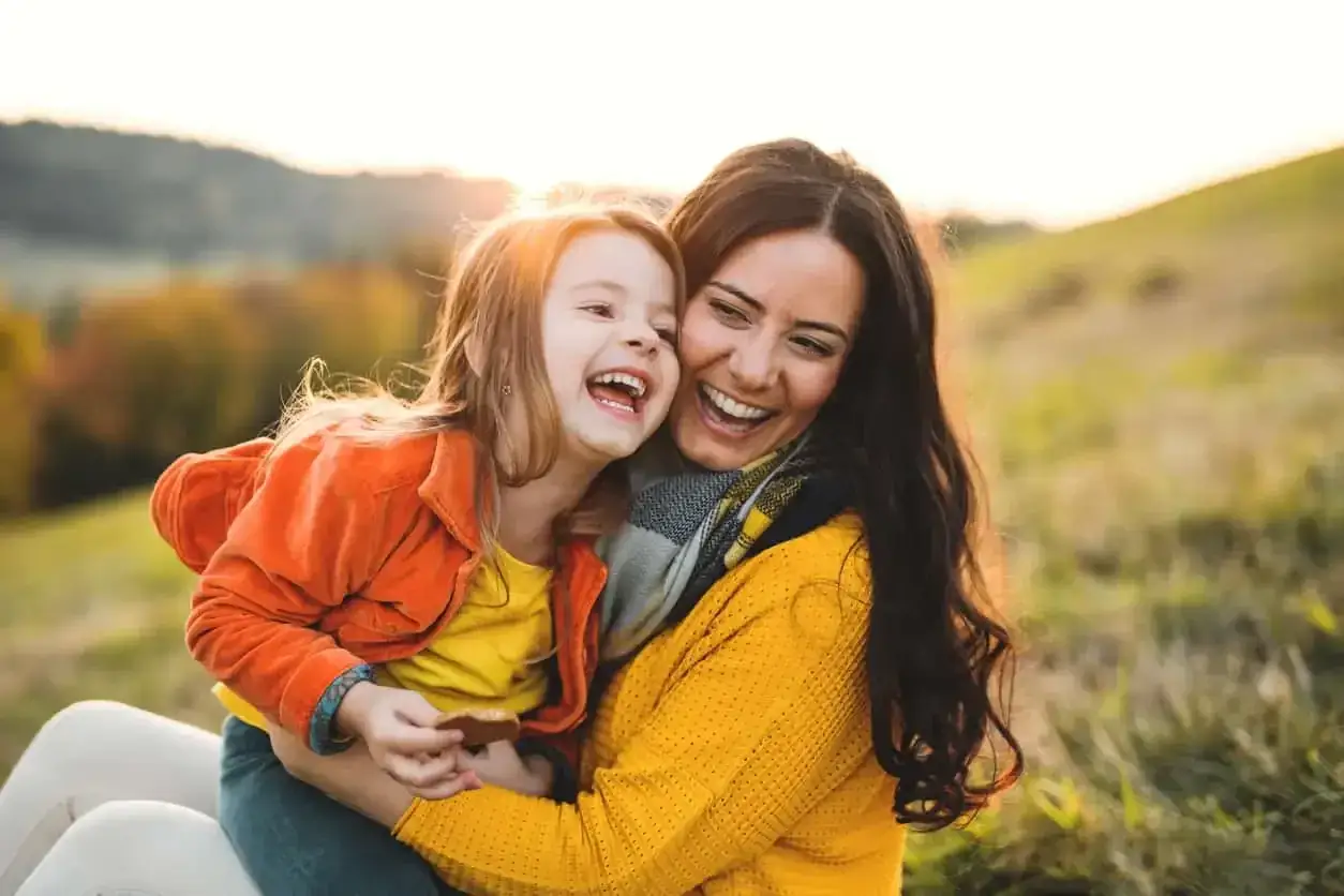 Uśmiechnięta mama i c&oacute;rka przytulają się na tle jesiennego krajobrazu. Ich radość potwierdza, że jaka matka taka c&oacute;rka cytaty.