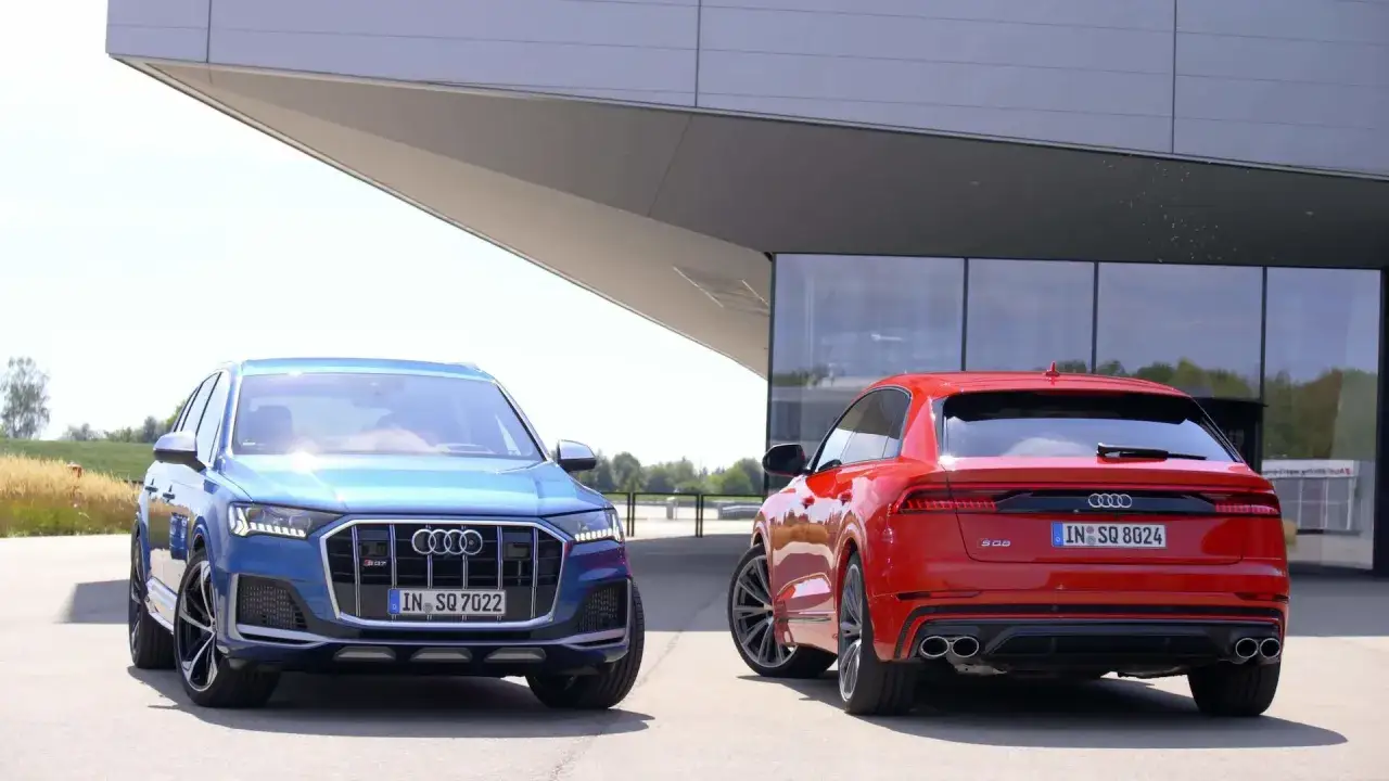 Dwa Audi: niebieski RS Q7 i czerwony SQ8 stoją obok siebie przed nowoczesnym budynkiem.