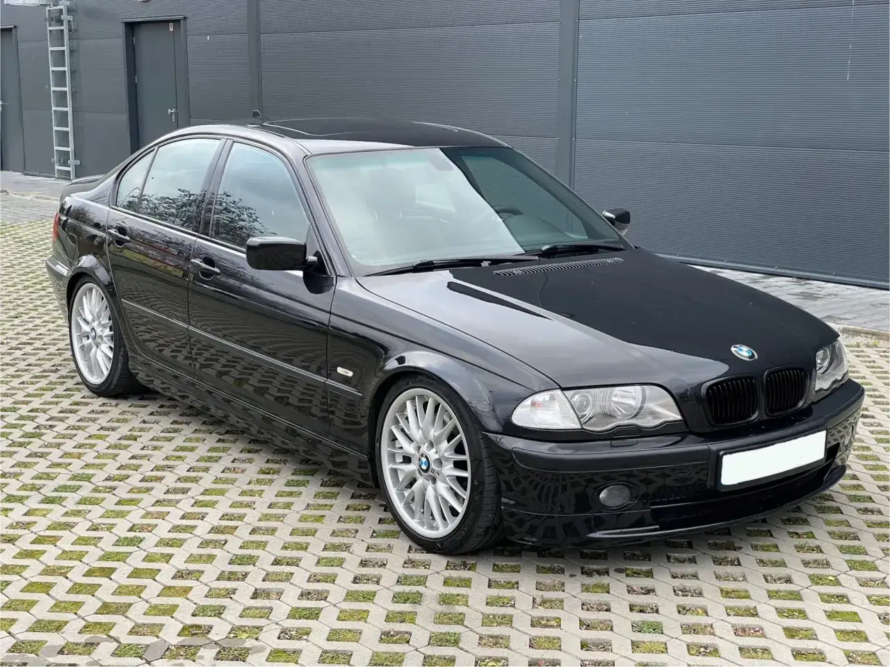 Lśniące czarne BMW E46 330i na betonowej nawierzchni z trawą. Klasyka motoryzacji.