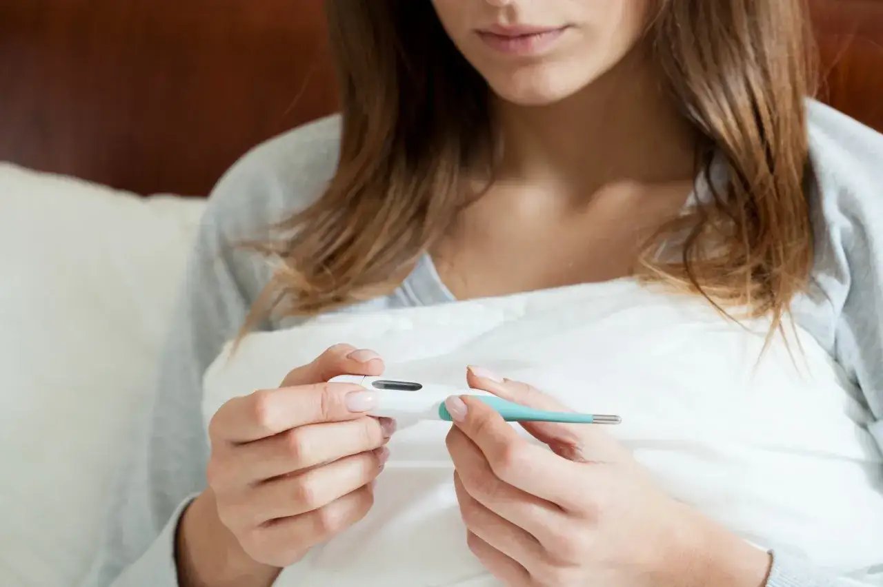 Kobieta zmartwiona patrząca na termometr i negatywny test ciążowy