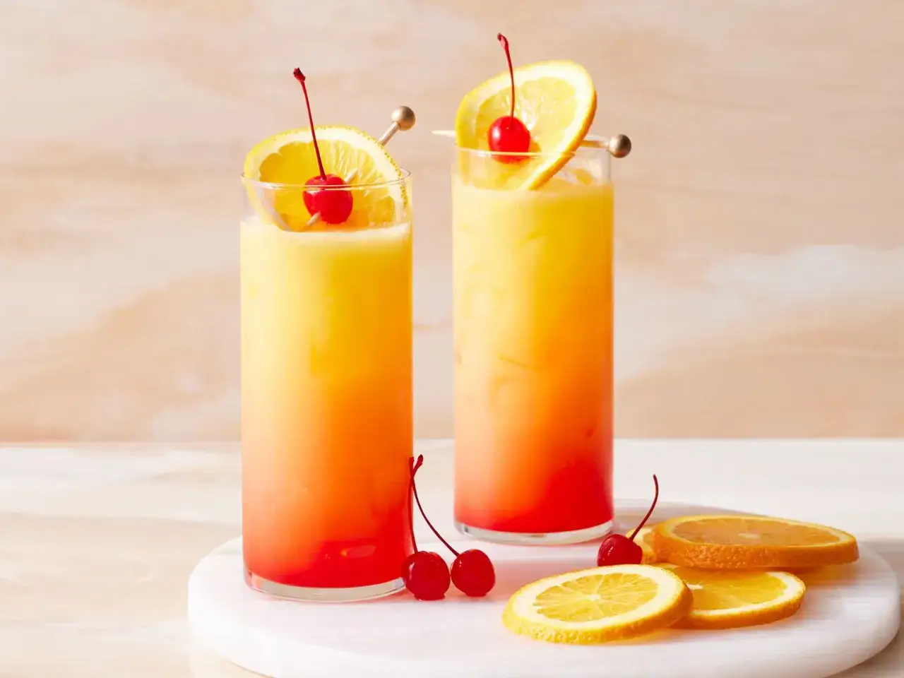 Dwa drinki Tequila Sunrise z pomarańczą i wiśnią, gotowe do podania.