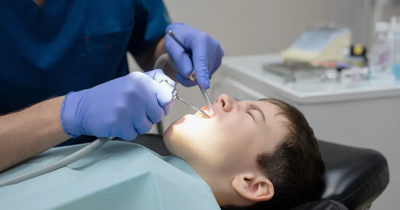 Chłopiec u dentysty, który używa narzędzi i anestetyków, by zabieg był bezbolesny.