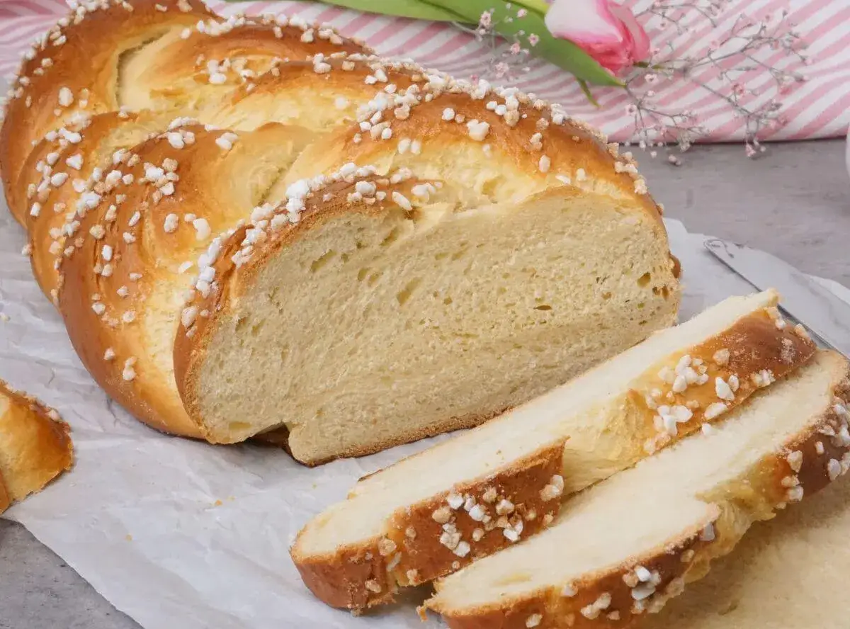 Ein goldbrauner Hefezopf, bestreut mit Zuckerkristallen, liegt angeschnitten auf Backpapier. Das Rezept für diesen Hefezopf ist einfach und gelingt immer.