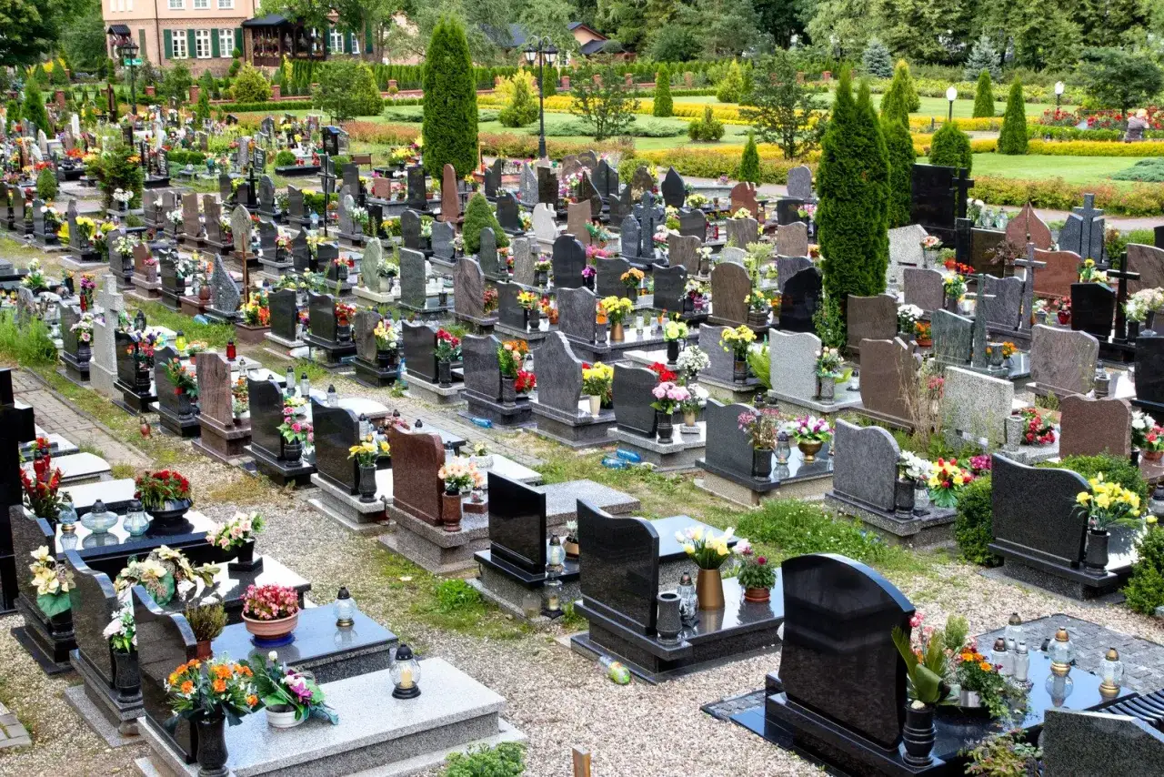 Cmentarz przygotowany do Święta Zmarłych. Groby ozdobione kwiatami i zniczami. Harmonogram prac obejmuje porządkowanie i dekorowanie nagrobków.