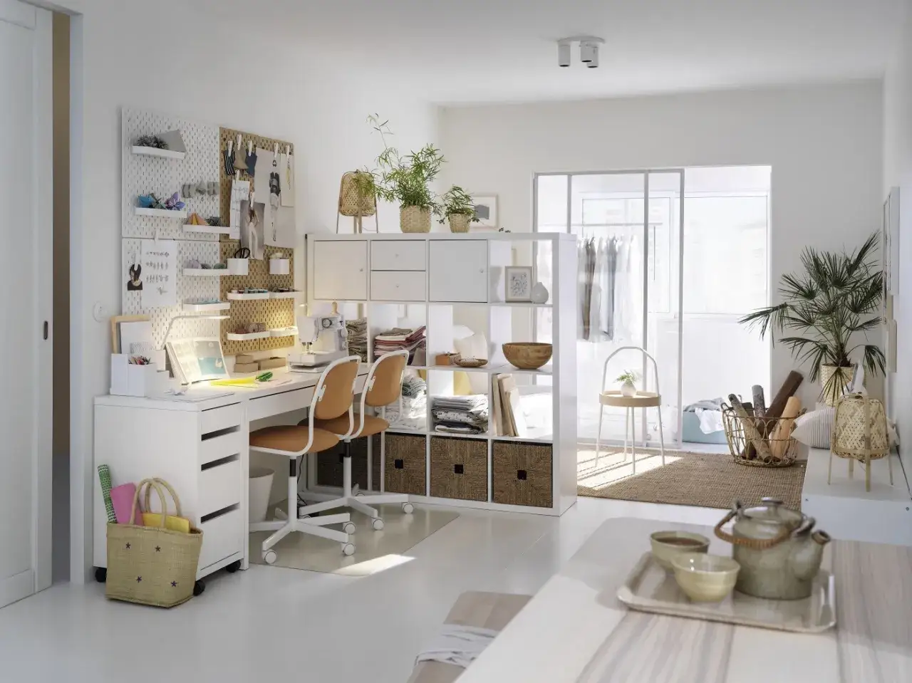 Kallax Ideen Arbeitszimmer: Ein helles Nähzimmer mit Schreibtisch, Nähmaschine, zwei Stühlen und einem Regal.