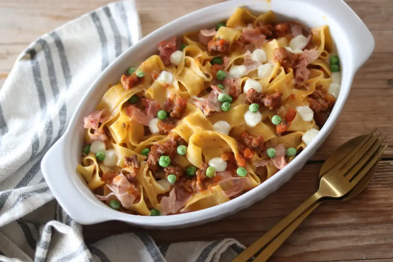 Nidi di tagliatelle al forno con ragù, piselli, mozzarella e prosciutto. Un piatto invitante pronto per essere gustato.