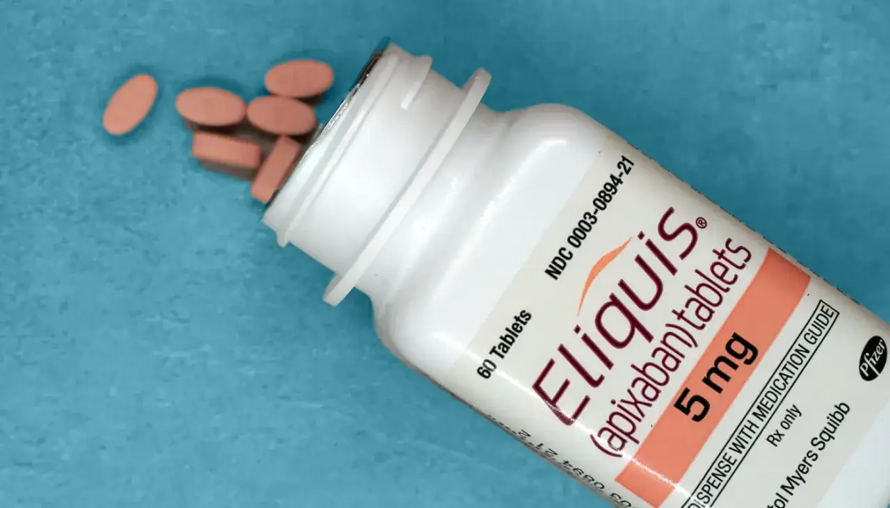 Tabletki Eliquis (apixaban) 5 mg wysypujące się z białej butelki na niebieskim tle.